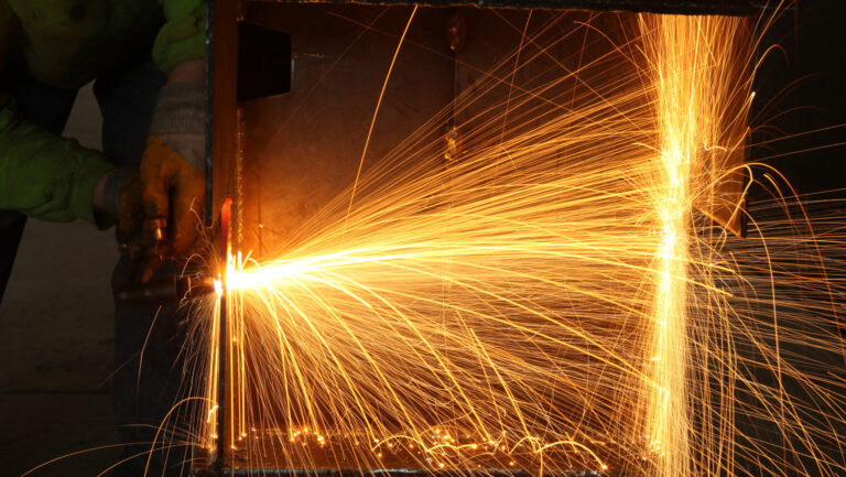 A worker uses a welding torch, producing bright orange sparks inside a metal structure—highlighting the importance of conducting an arc flash risk assessment to prevent electrical hazards in industrial environments.