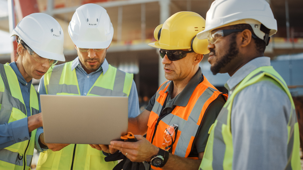 Diverse,Team,Of,Specialists,Use,Laptop,Computer,On,Construction,Site.