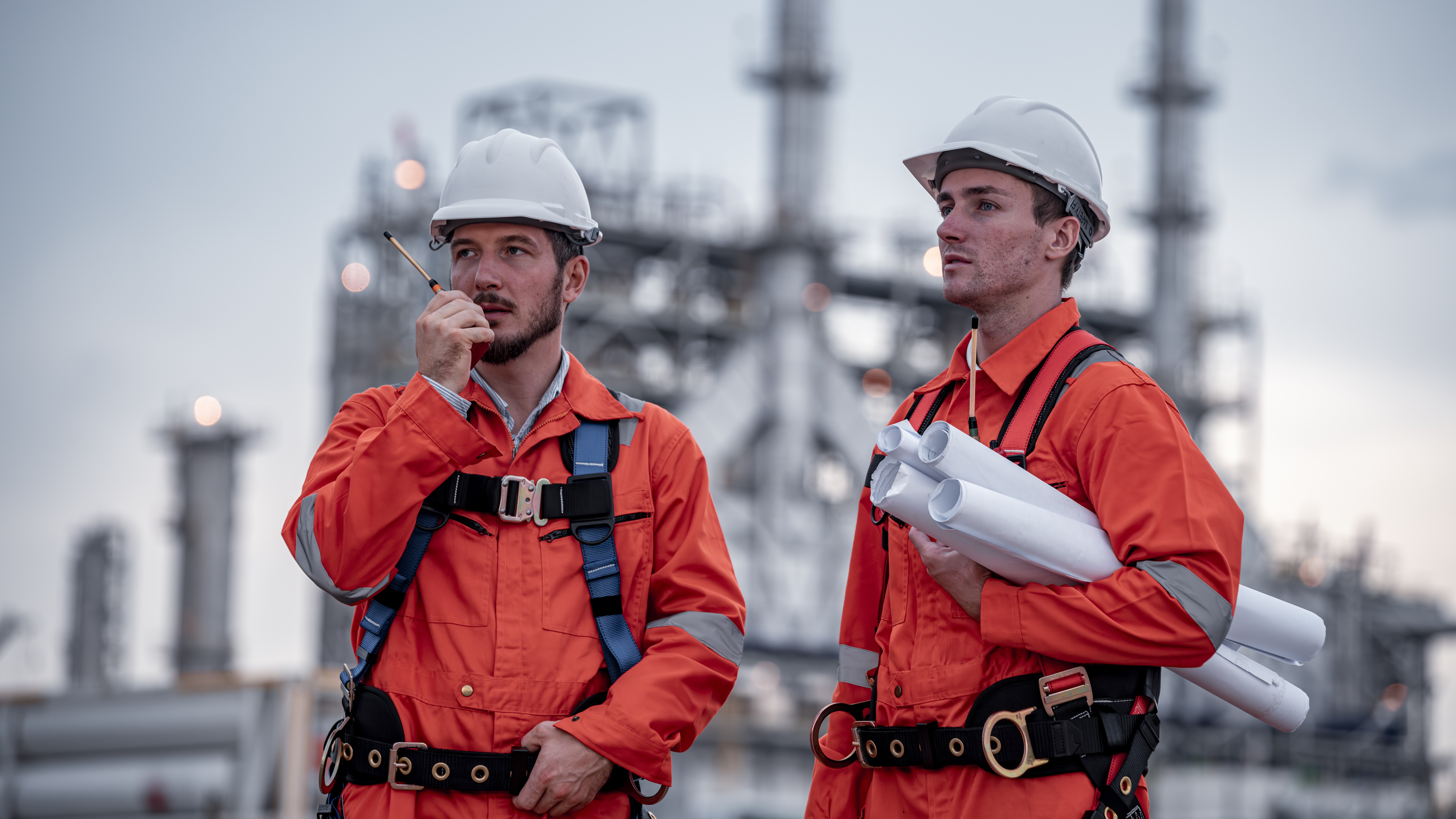 Two male engineers in bright orange clothes and safety harnesses, getting ready to share oil and gas safety toolbox topics.
