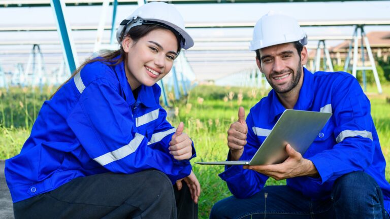 Female and male workers in bright blue high visibility vests and hard hats, installing solar panels outside according to spring safety tips and best practices.