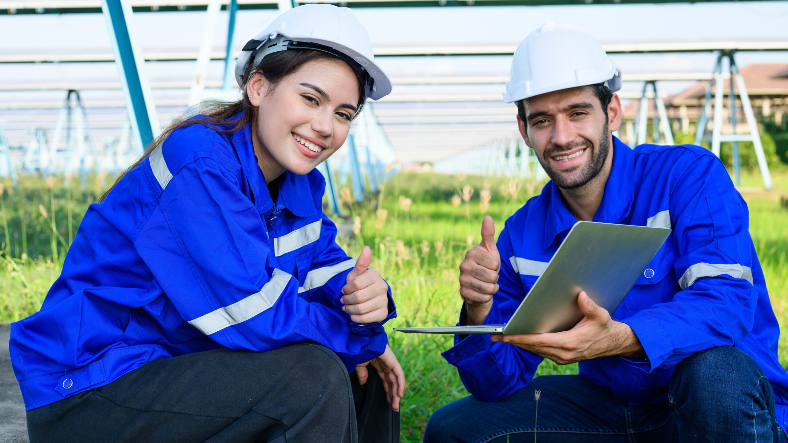 Female and male workers in bright blue high visibility vests and hard hats, installing solar panels outside according to spring safety tips and best practices.