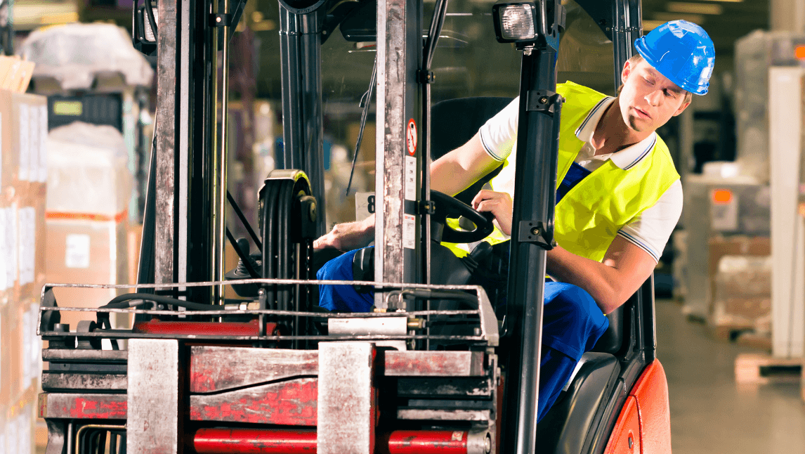 A warehouse worker operating a forklift looks over his shoulder while reversing, narrowly avoiding a collision—an example of near misses in a busy industrial environment