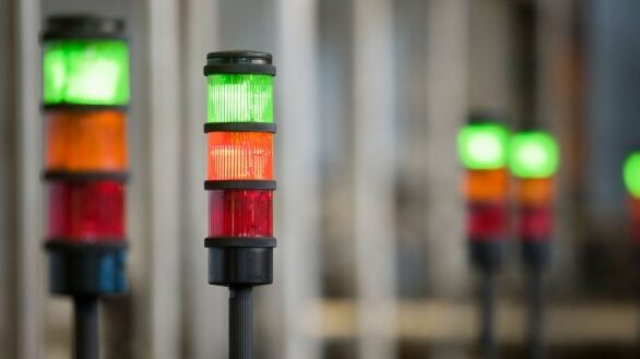 Industrial andon systems with stacked signal lights showing green, orange, and red indicators used to monitor production status on a factory floor.
