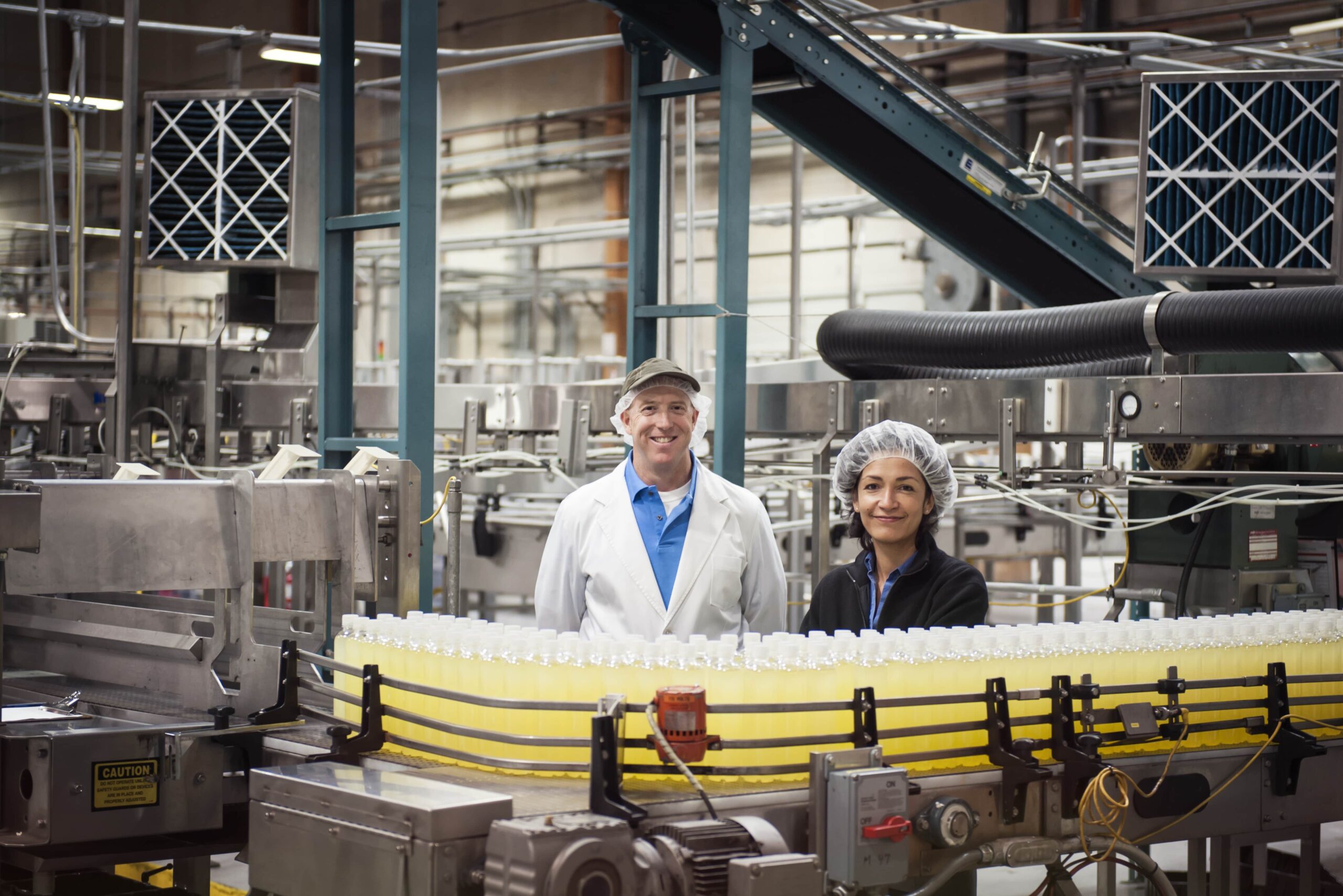 Male and female factory workers smiling next to a conveyor belt of food products