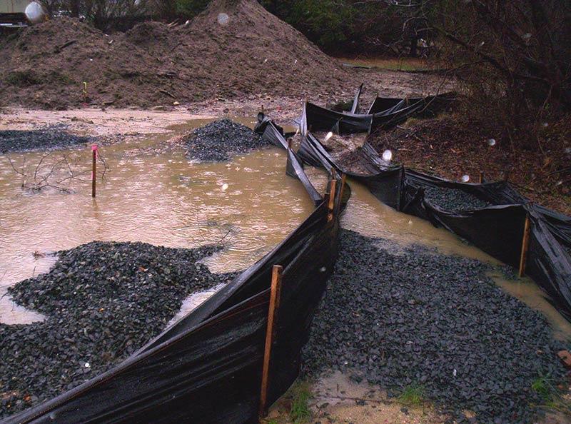 A flooded construction site with a stormwater bmp in place. It is a black plastic material set up with wooden posts so that water stops where the plastic hits the ground.