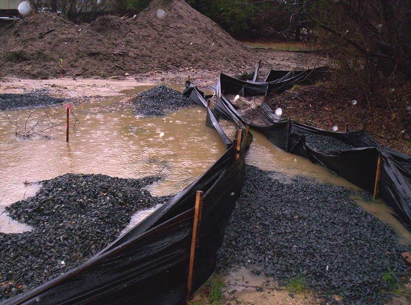 sediment control water runoff A flooded construction site with a stormwater bmp in place. It is a black plastic material set up with wooden posts so that water stops where the plastic hits the ground.