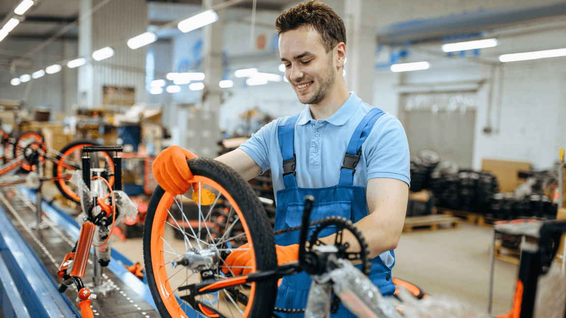 Worker assembling a bicycle in a factory setting, wearing safety gloves to prevent manufacturing hazards.