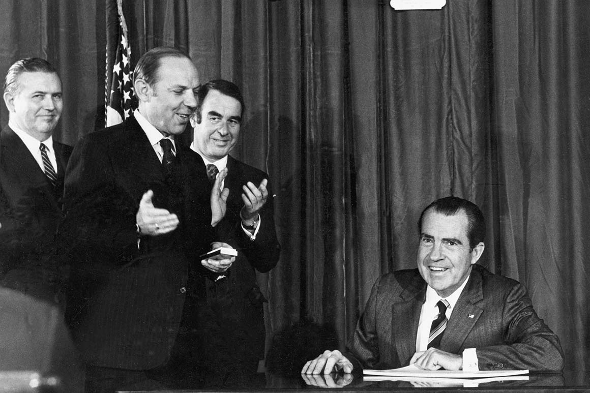 President Richard Nixon signs sitting down at a desk with the Occupational Health and Safety Act signed in front of him. Three government officials smile and stand off to the left. ehs software market context image