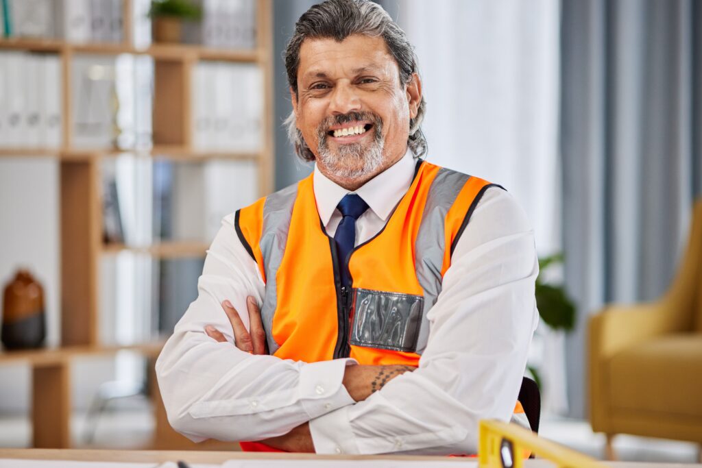 Confident construction manager wearing a safety vest and tie, smiling in an office setting, representing a change agent driving workplace improvements.