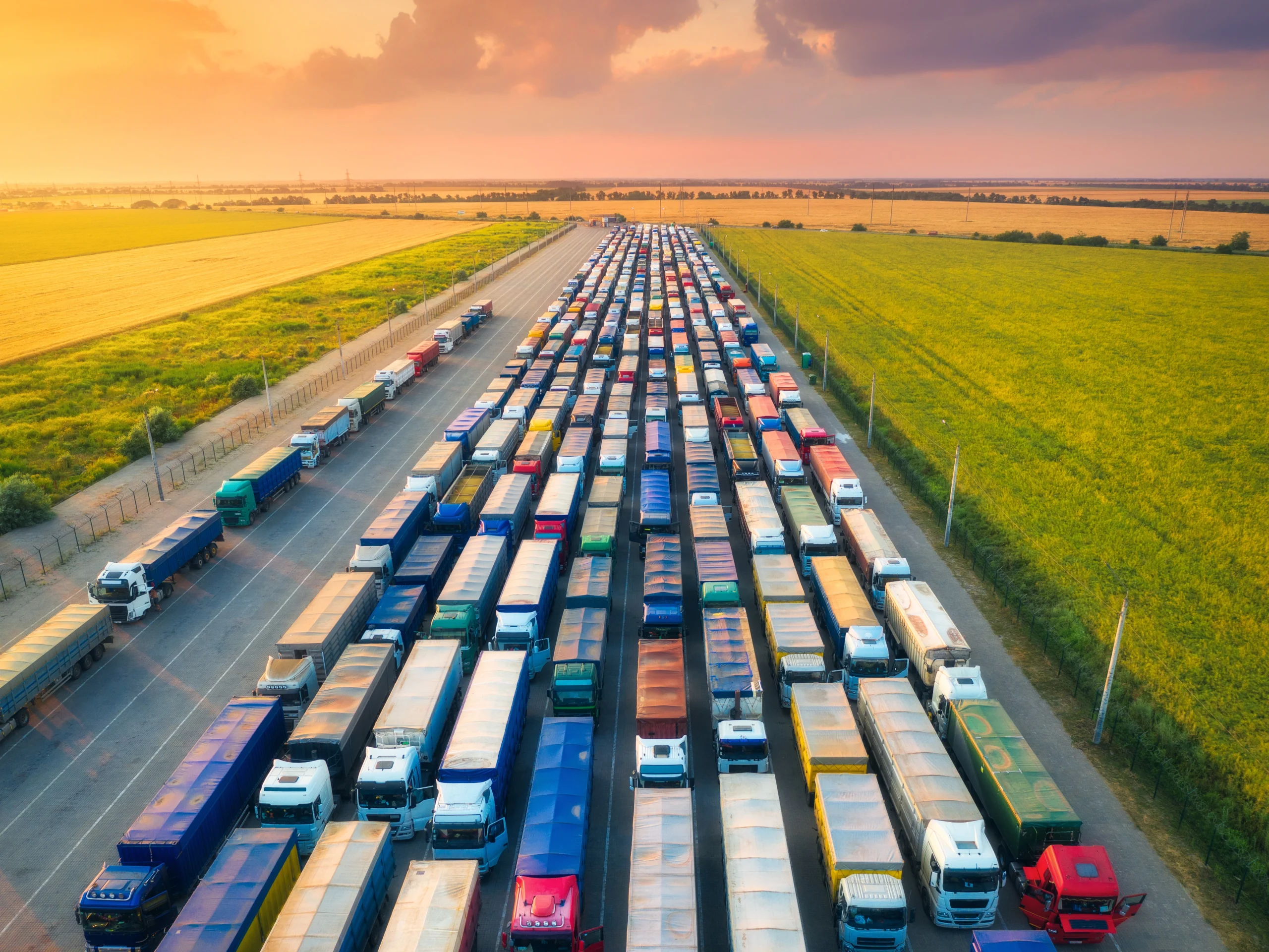 Aerial view of hundreds of commerical trucks lined up on a highway with green pastures on each side.