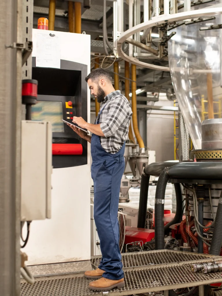 Male worker wearing blue overalls, boots, and a plaid shirt, doing an audit with EHS software for manufacturing companies.