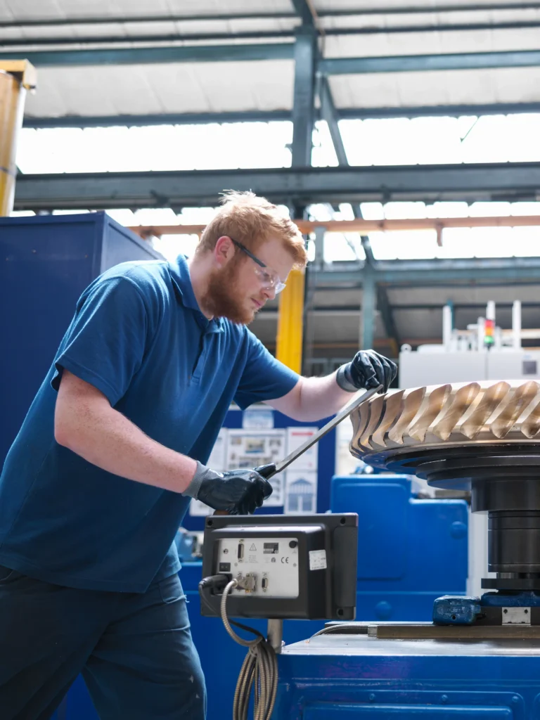 Male worker in blue shirt and safety glasses, wearing a blue t shirt and working on a piece of equipment.