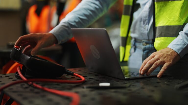 Close-up of a safety engineer in a high-visibility vest using a laptop and monitoring equipment in an industrial setting, illustrating how technology supports smarter safety decisions and improves workplace safety management.