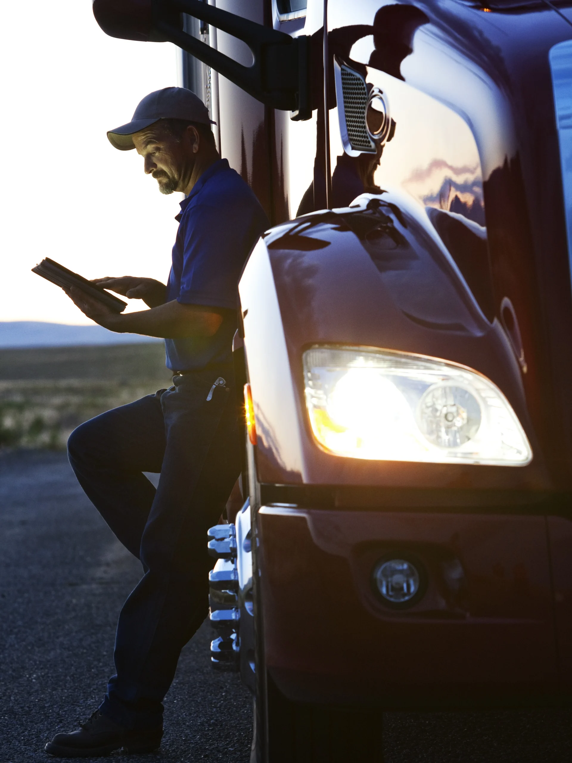Truck driver using transportation safety software to do a check before getting in his truck at sunset.