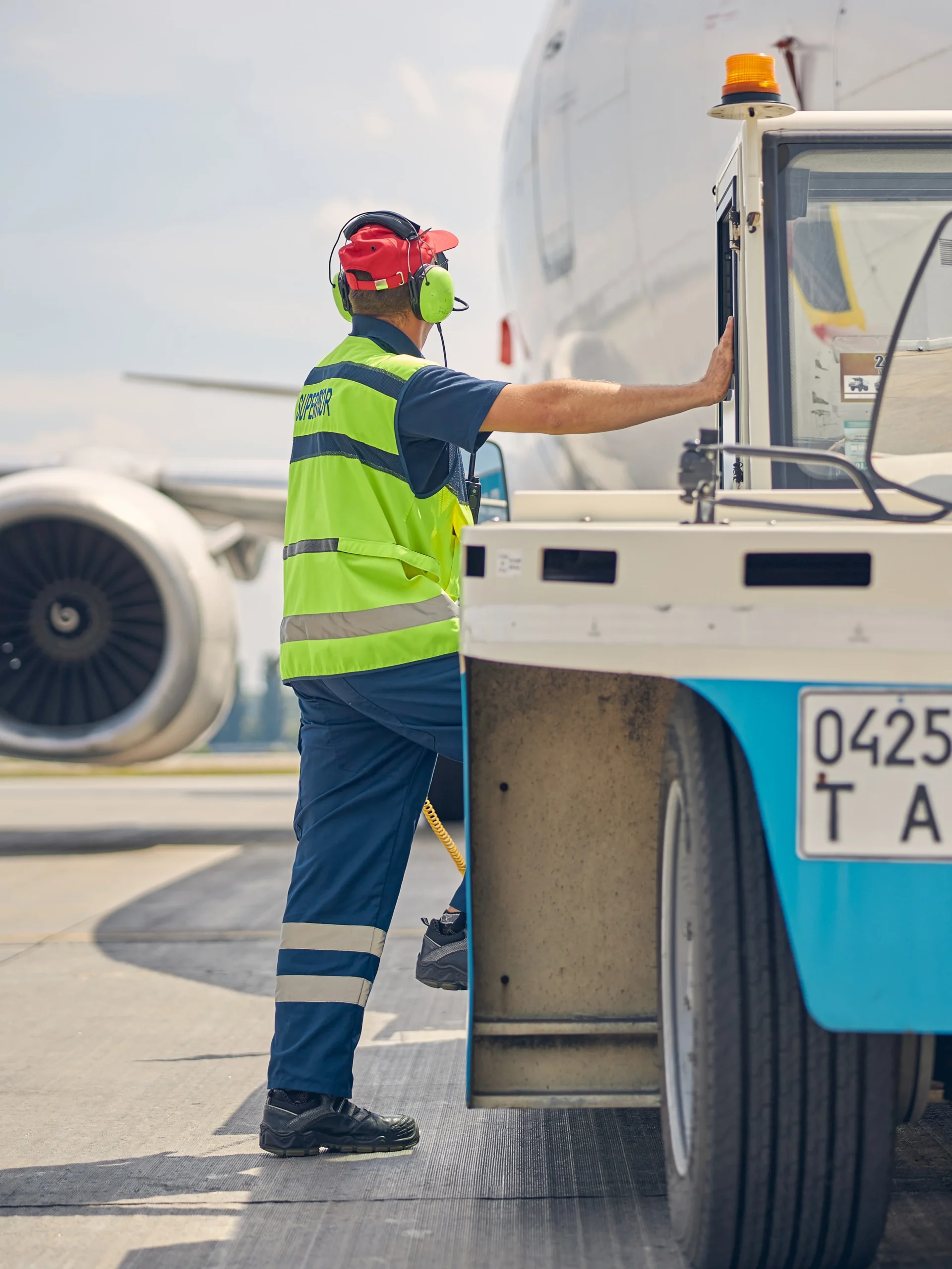 A male worker entering the cab of his tug equipment with an airplane in the background.