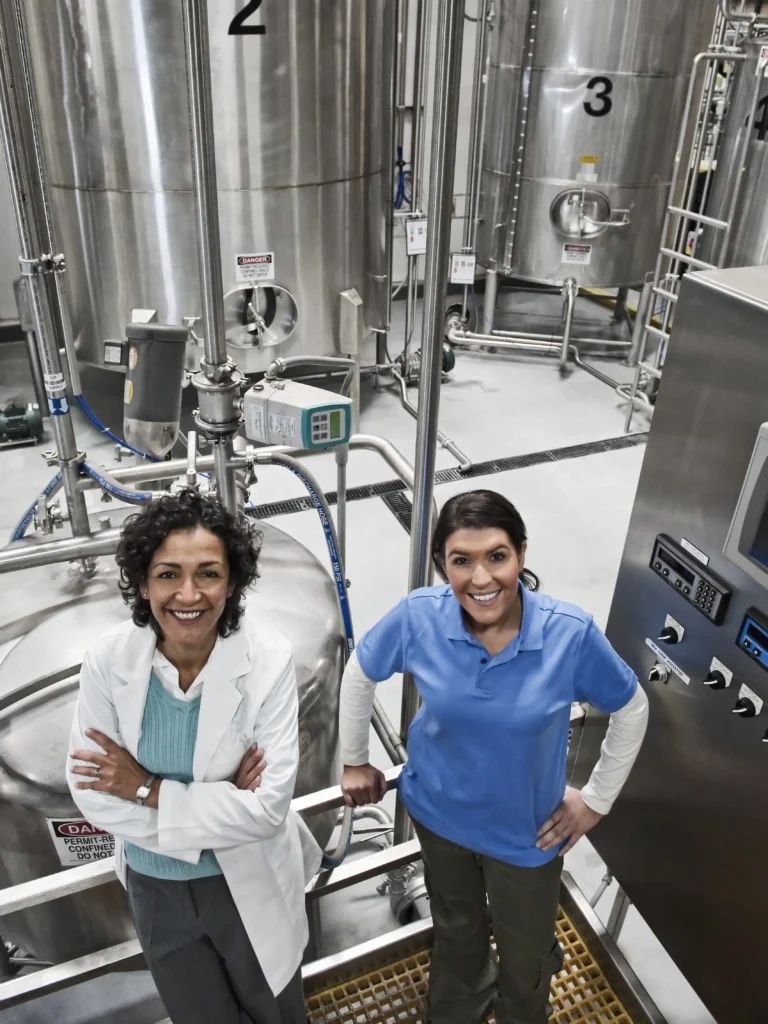 Two female workers smiling and standing in front of a large chemical storage container.