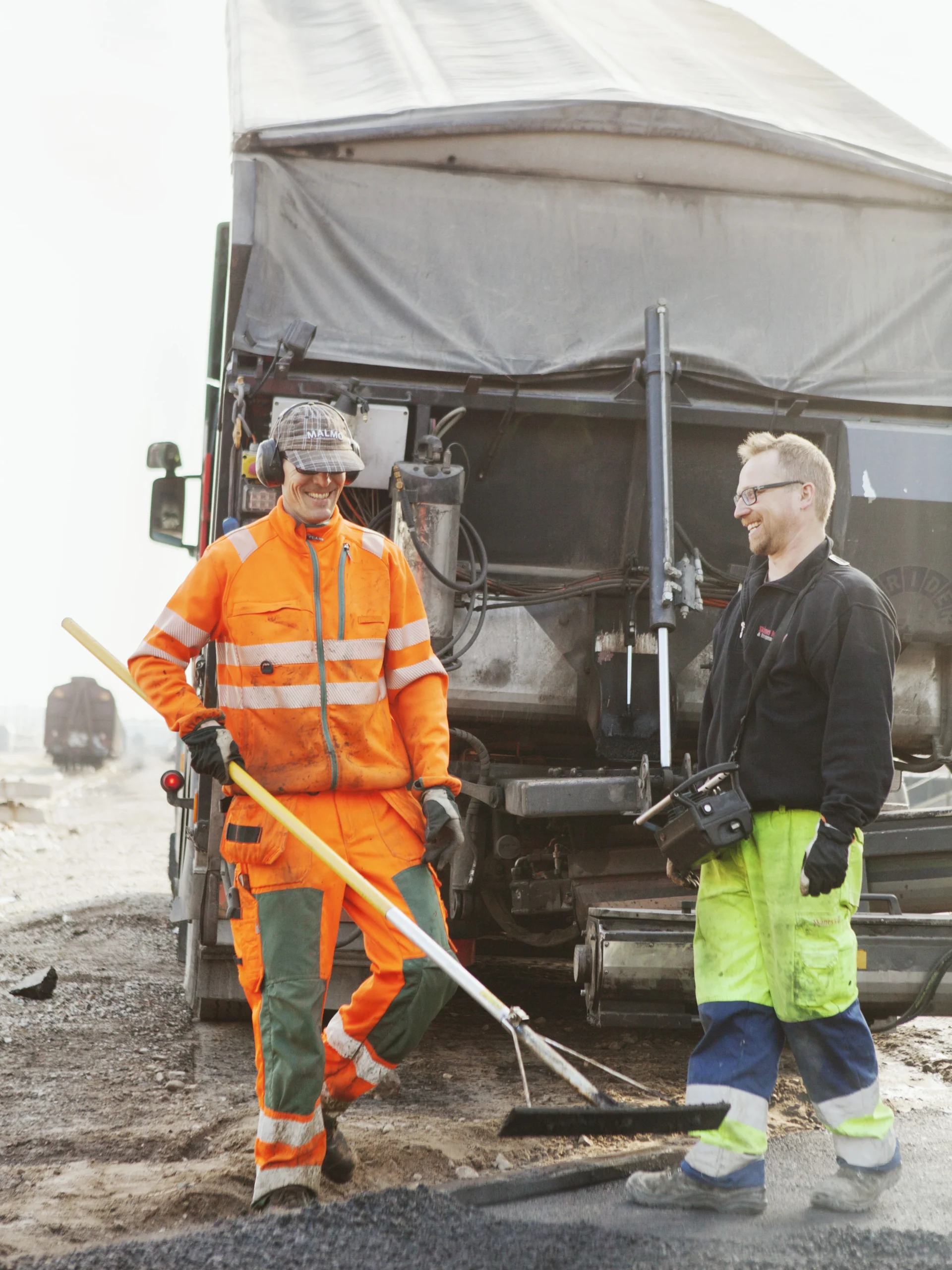 Two construction workers smiling and talking while pouring a new road.