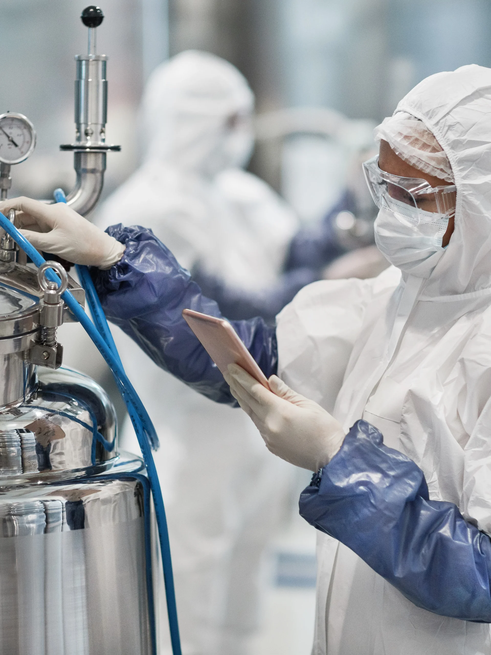 Worker in a chemical processing facility wearing full safety gear and conducting an audit with chemical safety software.