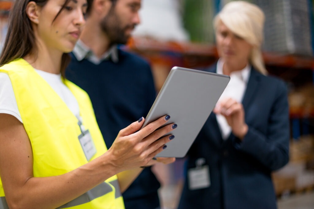 Warehouse safety manager using a tablet to review digital checklists while discussing with team, showing how efficient safety systems improve compliance and streamline operations.