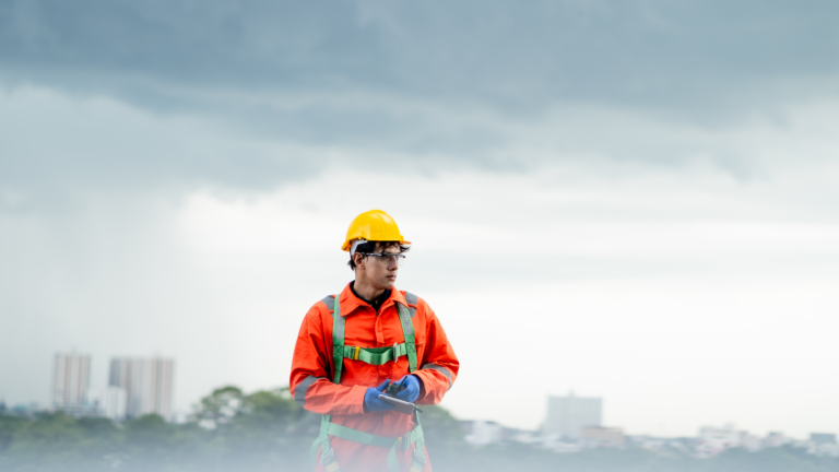 Male worker in yellow hard hat and orange safety suit working in inclement weather conditions